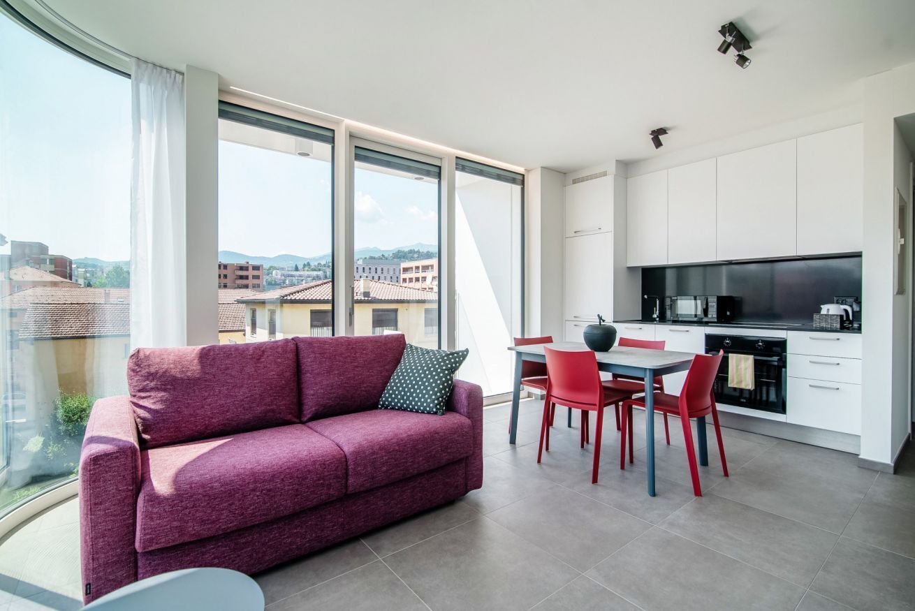 Een modern appartement met een eethoek, keuken en grote ramen met uitzicht op de stad.