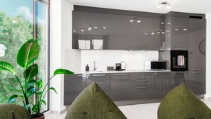 Una cocina moderna con armarios oscuros, un microondas y una cafetera. Hay dos sillas verdes y una planta grande cerca de la ventana.