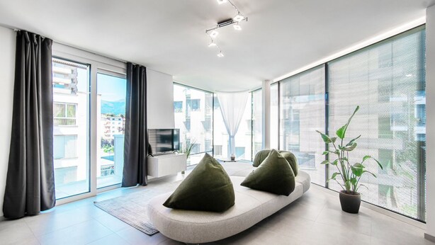 Una sala de estar moderna con un sofá curvo, un televisor de pantalla plana y un ventanal con vistas a la ciudad.