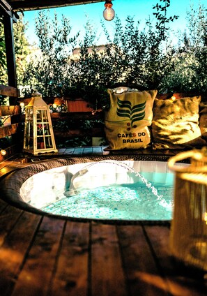 Un jacuzzi con terraza de madera, rodeado de plantas en macetas y un farol.