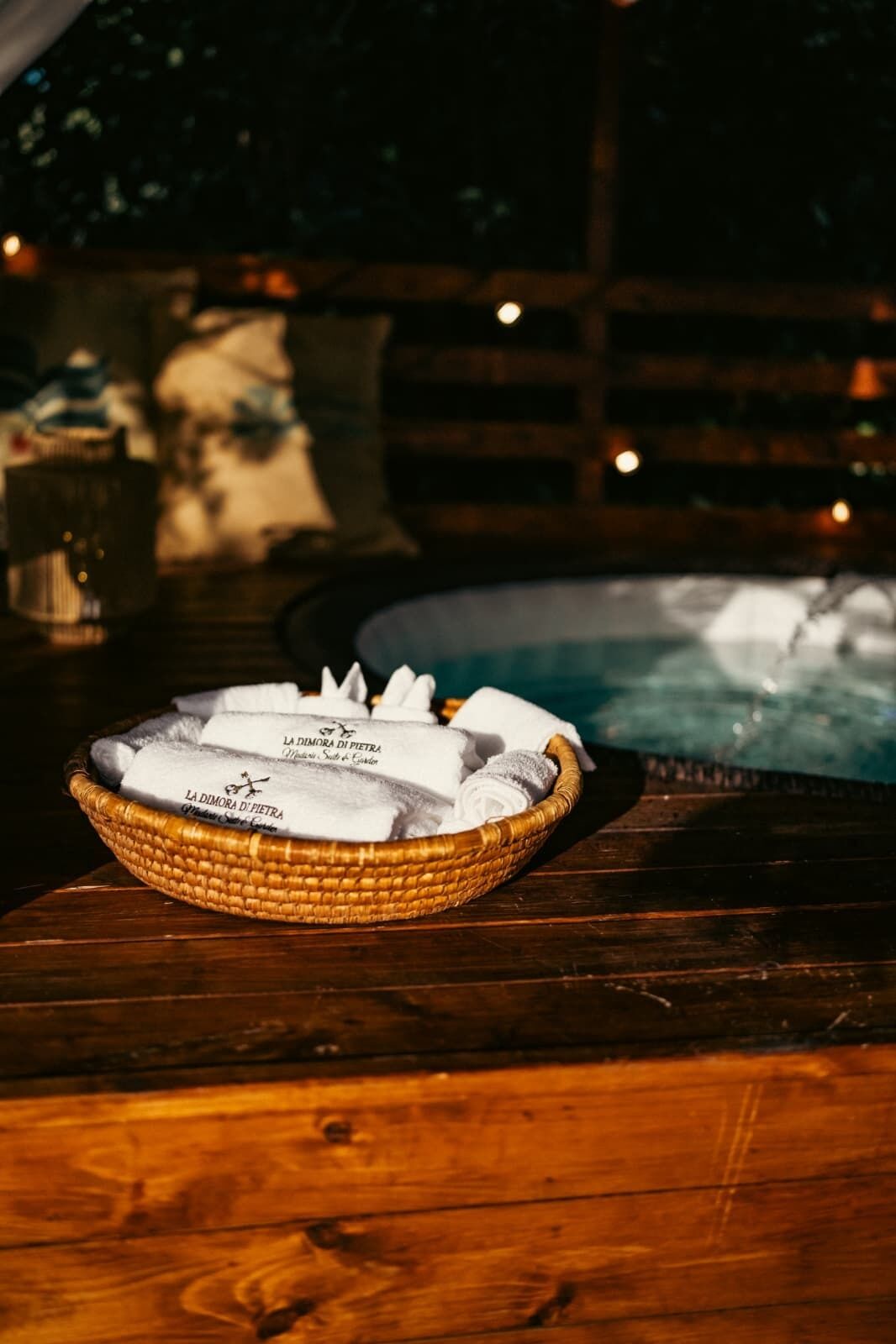Un panier en osier rempli de serviettes pliées, posé sur une table en bois près d’une piscine.