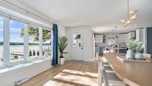 Ett modernt kök med en stor köksö, en matplats med ett långt bord och utsikt över en sjö genom stora fönster.
