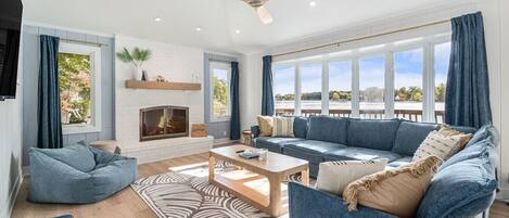 A spacious living room with a fireplace, large windows, and a view of the outdoors.