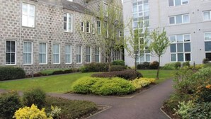 A courtyard with stone buildings, a paved walkway, and well-maintained shrubbery. - Central 2-bedroom flat with private parking in Aberdeen (Aberdeen)