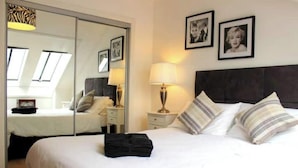 A hotel room with a large bed, a nightstand with a lamp, a wardrobe, and two framed pictures on the wall. - Central 2-bedroom flat with private parking in Aberdeen (Aberdeen)