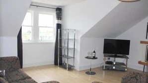 A living room with a TV, a glass shelf, and patterned sofas. - Central 2-bedroom flat with private parking in Aberdeen (Aberdeen)