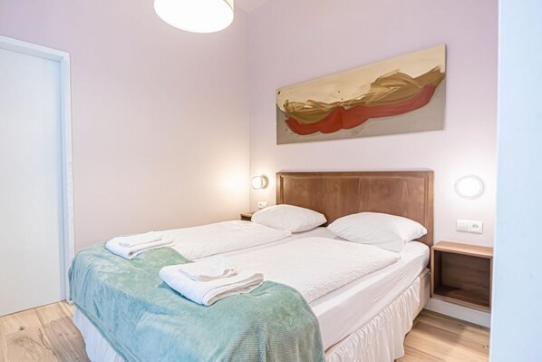 A bedroom with two beds, a wooden headboard, bedside tables with lamps, and a painting on the wall. - Stylish Aparthotel | 1 Room+Lounge by Mariahilfer (Vienna)