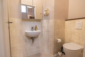 A bathroom with a sink, mirror, hairdryer, toilet, and patterned tiles. - Stylish Aparthotel | 1 Room+Lounge by Mariahilfer (Vienna)