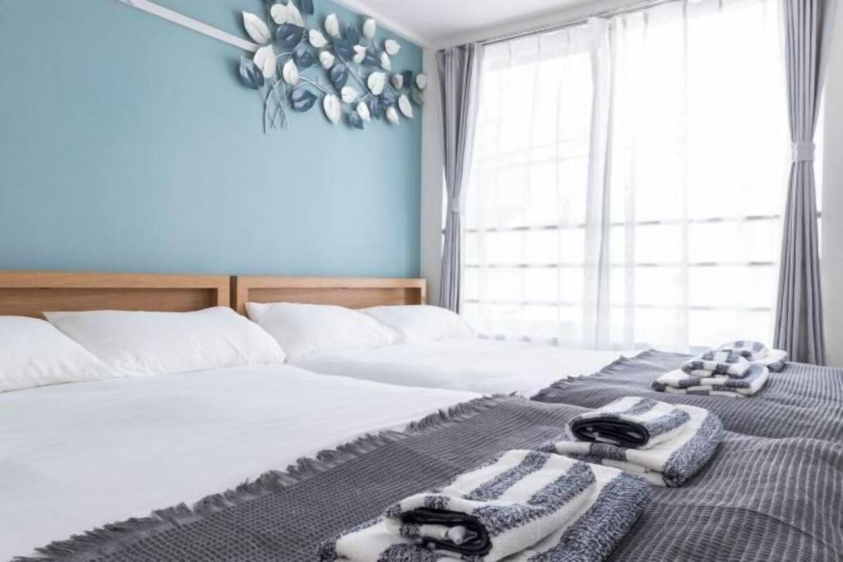 A hotel room with two beds, a wooden headboard, a wall art piece, and a large window with curtains.
