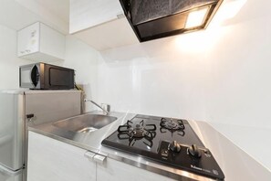 A modern kitchen with a stainless steel sink, a black stove, and a microwave on the countertop. - Tsubaki　202 (Tokyo)