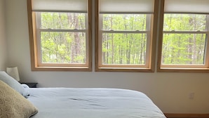 Un dormitorio con cama, mesita de noche y tres ventanas con persianas.
