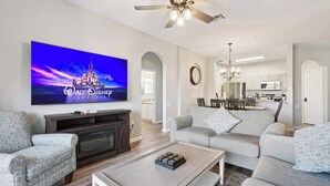 A living room with a flat-screen TV displaying 'Walt Disney Pictures', a ceiling fan, a dining area with a chandelier, and a kitchen in the background. - Updated 3BR Monsters Inc themed condo with Water Park near Disney (Kissimmee)