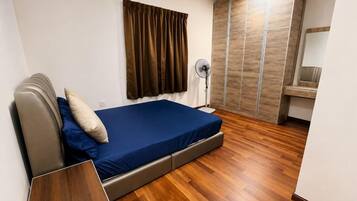 A bedroom with a bed, a bedside table, a standing fan, and a wardrobe.
