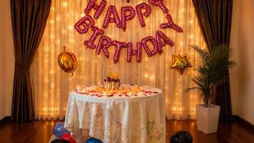 A room with a table set for a birthday celebration, featuring a 'HAPPY BIRTHDAY' balloon arch, a table with a white tablecloth, and balloons on the floor.