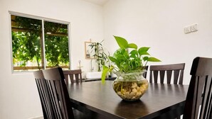 Una mesa de comedor con sillas, un florero con plantas y un ventanal con vista a árboles.