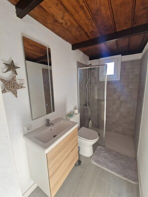 Une salle de bain avec un plafond en bois, un lavabo blanc, des toilettes et une cabine de douche en verre.