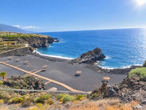Eine Küstenlandschaft mit felsigem Strand, klarem, blauem Meer und einem gebirgigen Hintergrund.