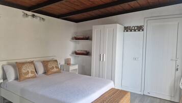 Un dormitorio con cama, una banca, un armario y estanterías con cestas.