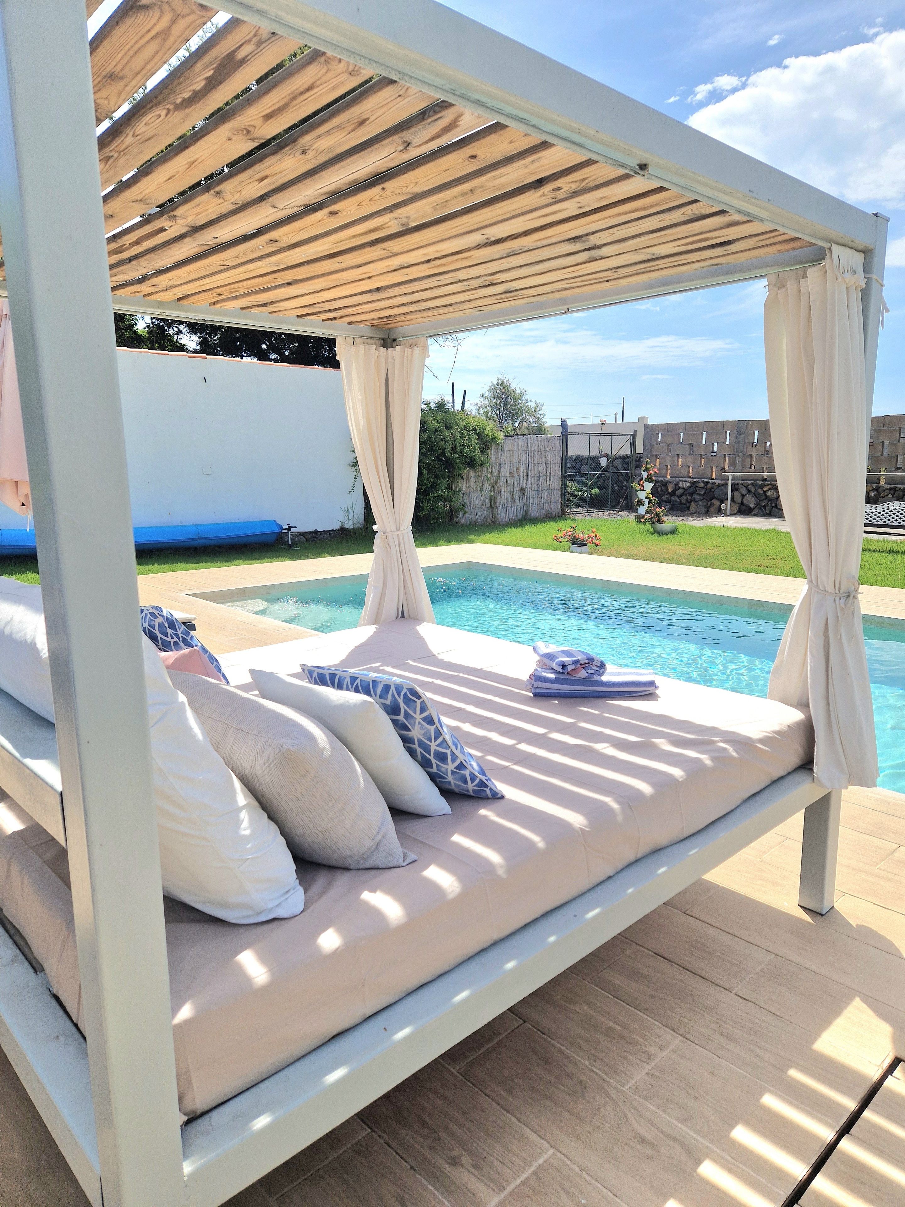 A poolside bed with a canopy, a pool, and a stone wall in the background.