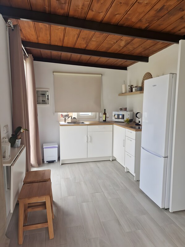Una cocina compacta con armarios blancos, techo de madera, refrigerador blanco y microondas en la encimera.