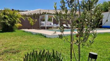 Un jardín con un parterre de cactus, una banca y una zona de piscina con sillones de descanso.