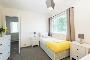 A bedroom with a bed, bedside tables, a dresser, a window with curtains, and a door leading to another room. - Toast Stays - Broomfield House (Durham)