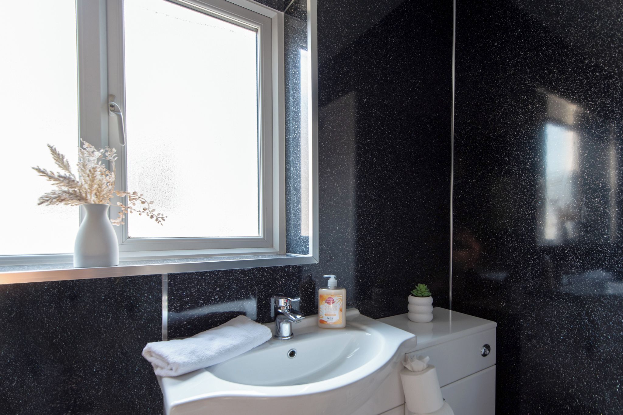 Ein Badezimmer mit einem weißen Waschbecken, einem Fenster und einem Spiegel.