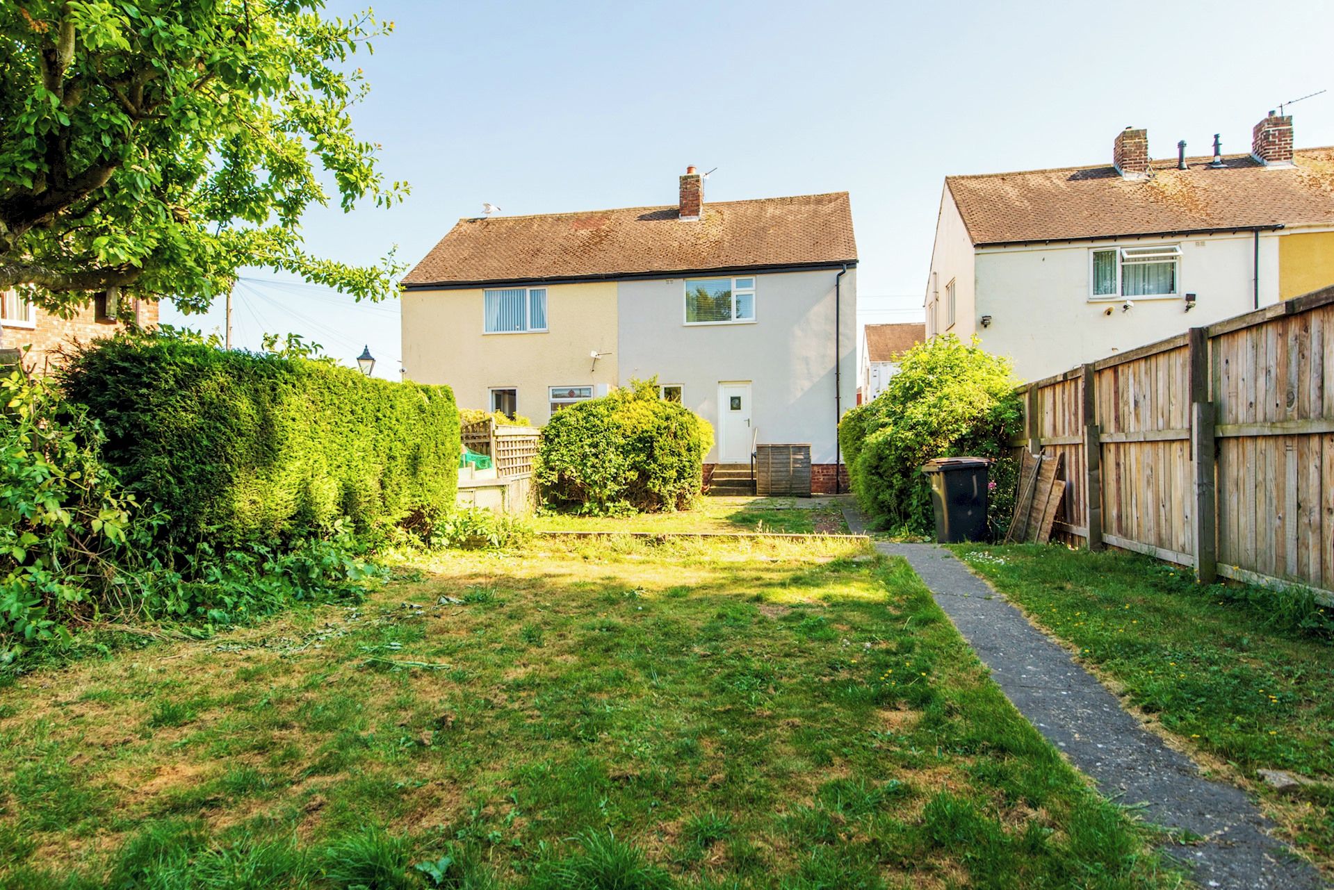 A residential area with two houses, a grassy yard, and a wooden fence.