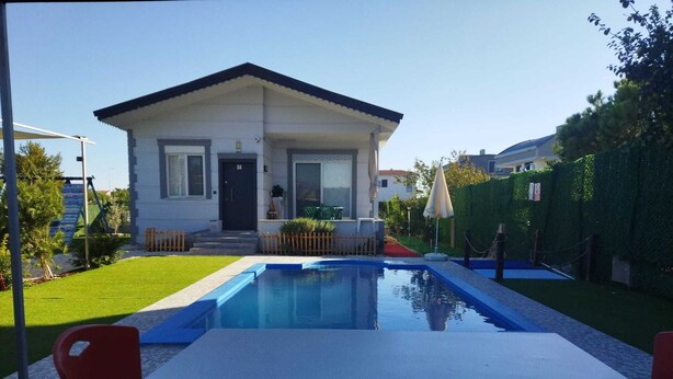 A house with a swimming pool, a patio table, and red chairs.