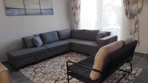 A living room with a sectional sofa, a black armchair, a patterned rug, and a painting on the wall.