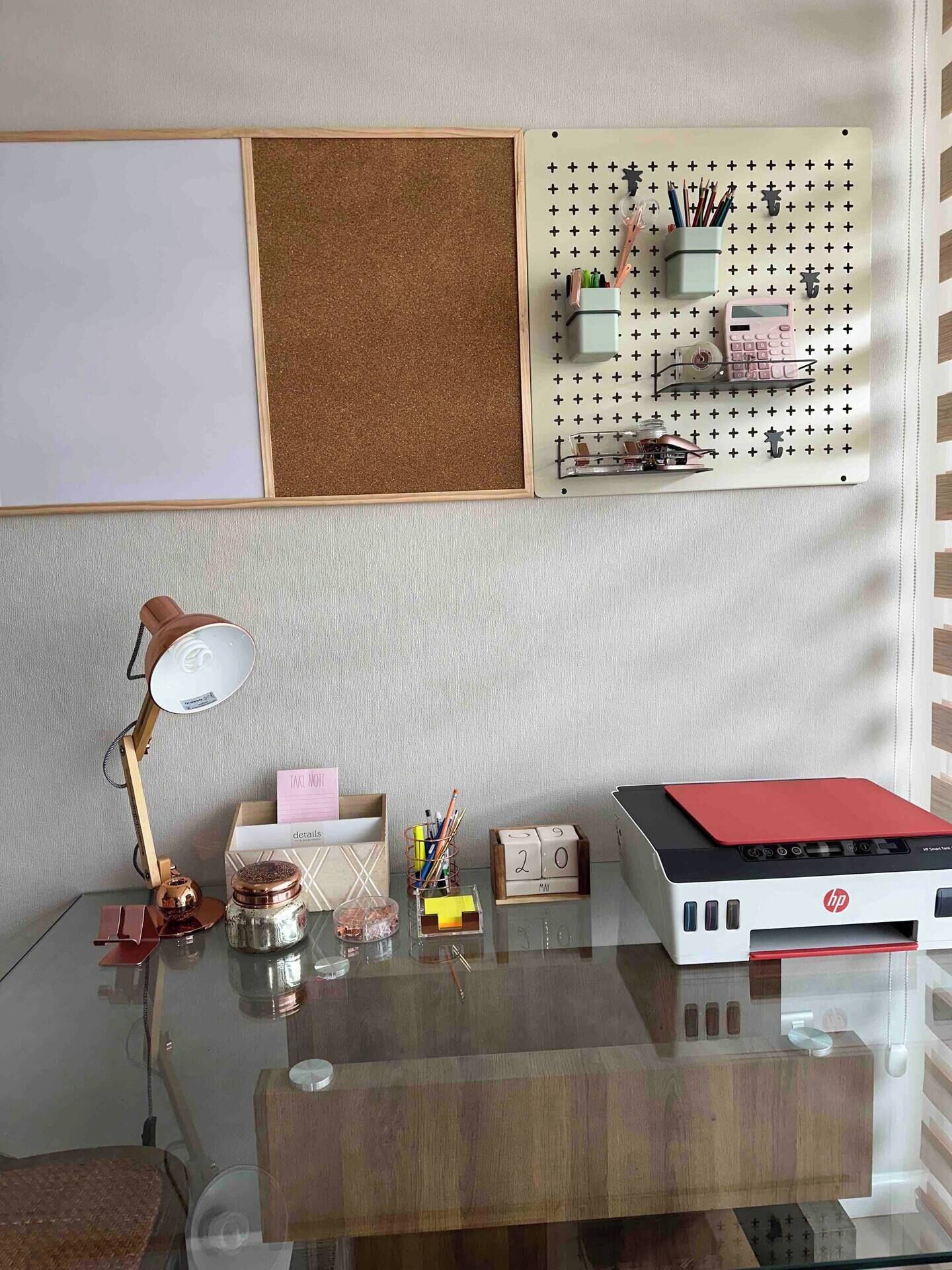 Un espace de travail bien organisé, comprenant un tableau d’affichage en liège, un panneau perforé, une lampe de bureau et une imprimante HP.