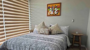 A bedroom with a bed, pillows, a small table, and a painting on the wall. - Trabajo y Relax VIP en La Serena (La Serena)