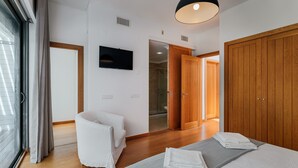 Habitación de hotel moderna con una cama, una silla blanca, un televisor y un armario de madera.