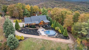 A lodge with a large deck, a hot tub, and a pool, surrounded by autumn foliage and mountains. - Heated Pool, Spa, Theater & Mountain Views, 6 King en suites – Sleeps 20 (Mineral Bluff)