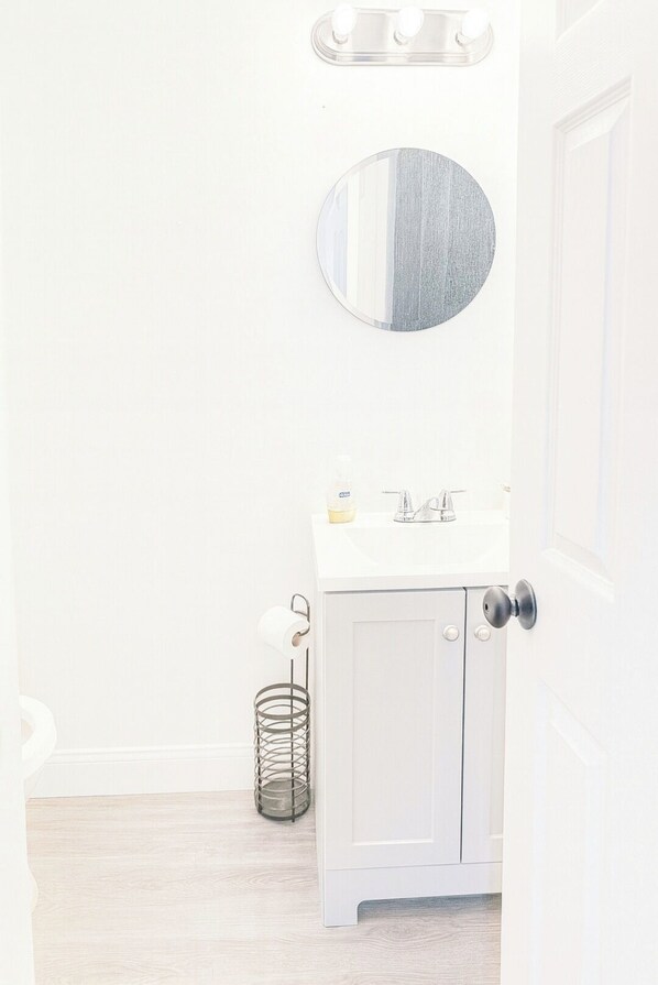 Une salle de bain avec un meuble-lavabo blanc, un miroir rond et un luminaire placé au-dessus du miroir.