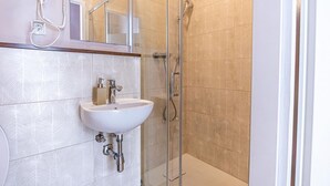 A bathroom with a white sink, a hairdryer, and a glass shower enclosure. - Modern Room with Private Bath | Mariahilferstraße (Vienna)