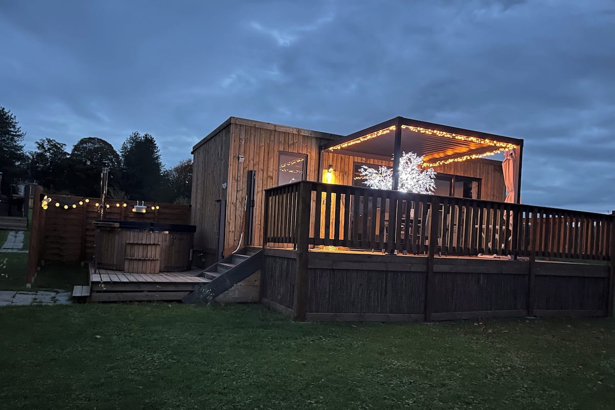 A wooden deck with a staircase leading to a covered area, surrounded by a wooden fence and string lights.