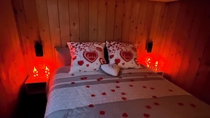 Una cama con pétalos de rosa, almohadas con diseño de corazón y cabecera de madera.