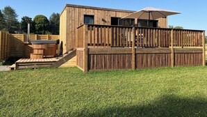 Una cabaña de madera con terraza, jacuzzi y pérgola.