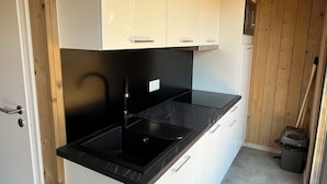 Cocina compacta con armarios blancos, encimera negra y techo de madera.