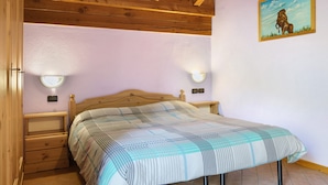 Een slaapkamer met een houten plafond, een bed met een beddeken met dessin, twee wandlampen en een schilderij van een paard.