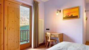 Ein Schlafzimmer mit einem Bett, einem Holztisch, einem Stuhl, einem Fenster mit Bergblick und einem Bild an der Wand.