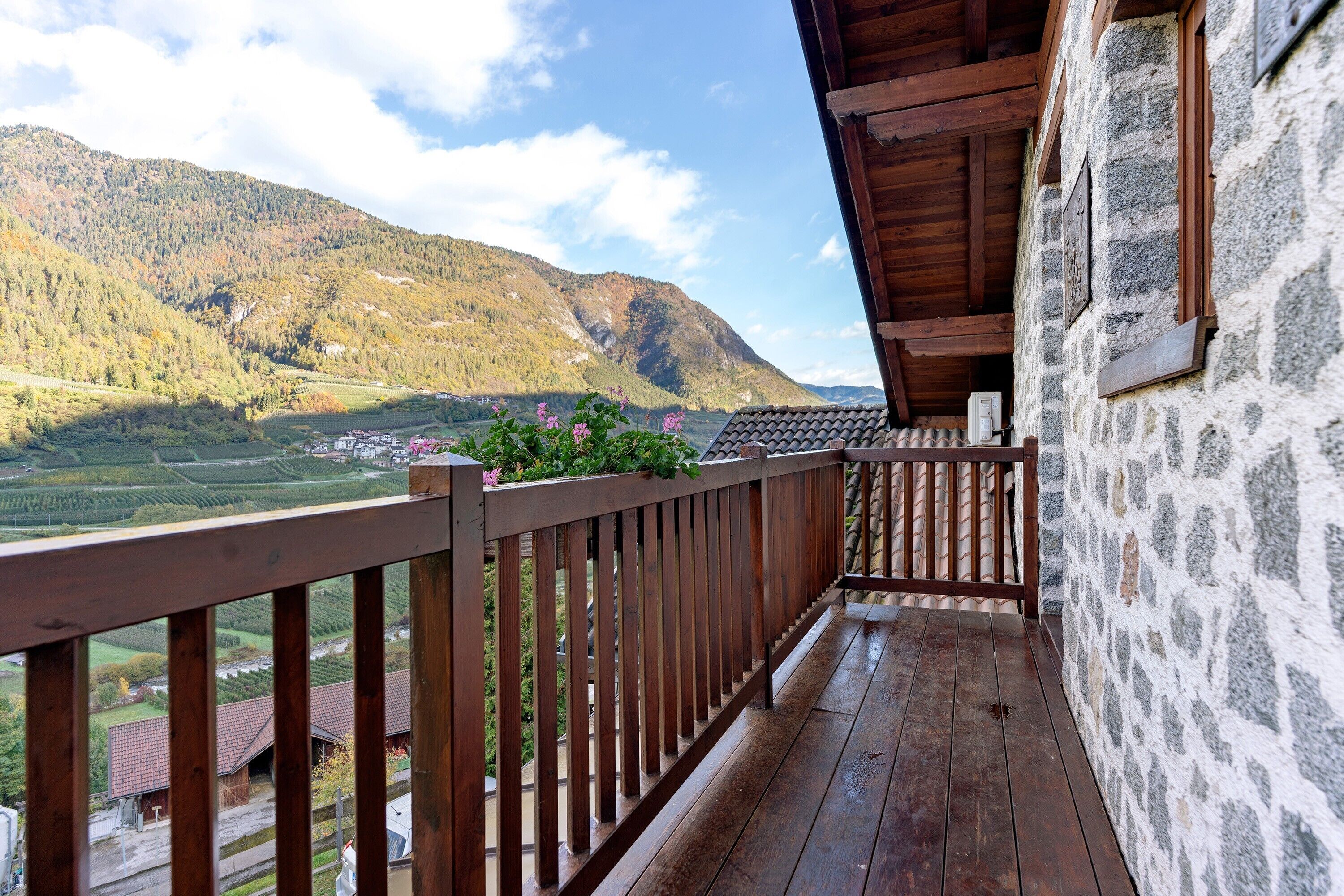 A wooden balcony with a stone wall, overlooking a mountainous landscape.