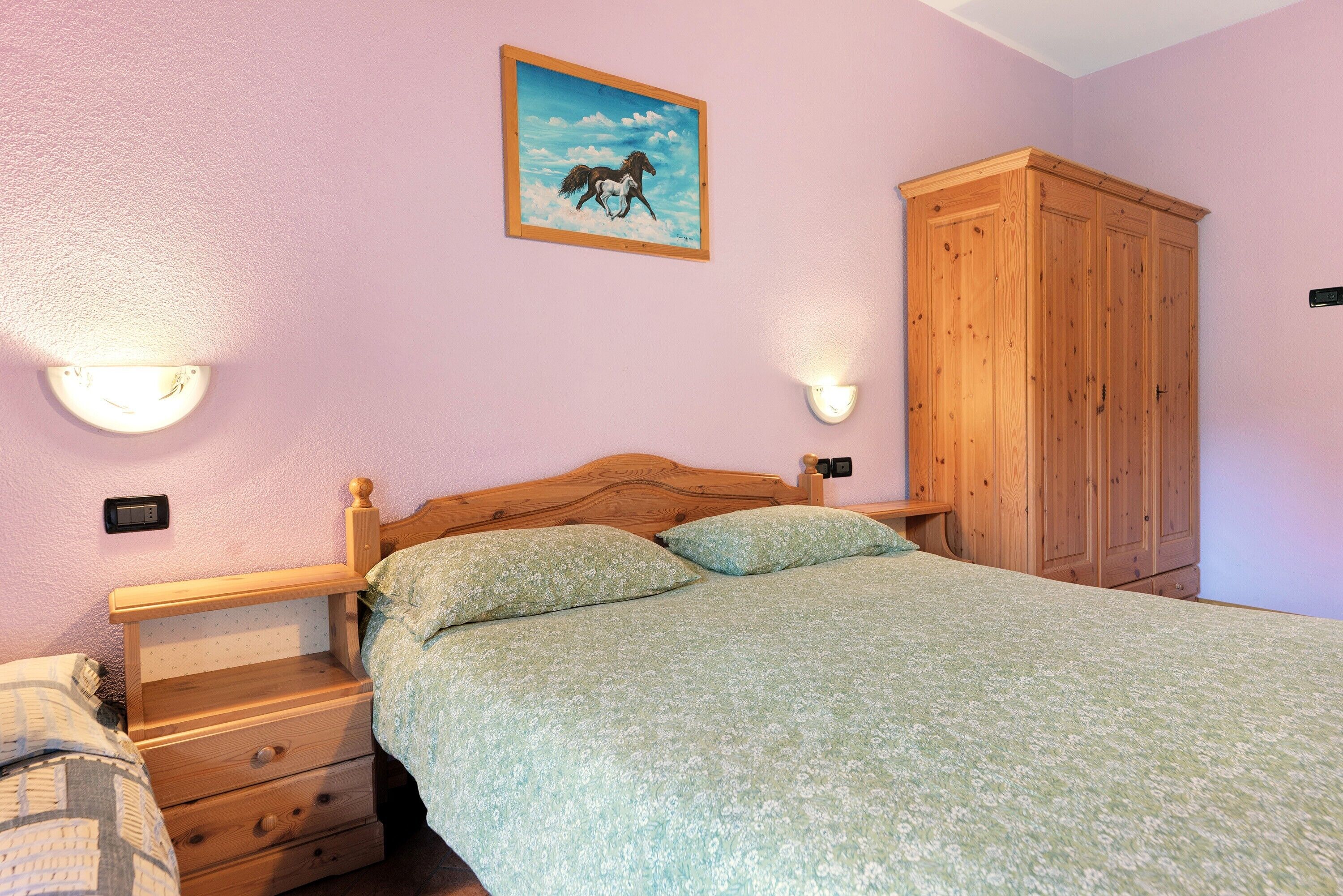 Un dormitorio con una cama de madera, una mesita de noche, un armario de madera y una lámpara de pared.