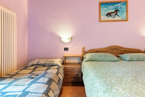 Une chambre avec deux lits, une table de chevet, une lampe fixée au mur et un tableau.