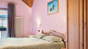 Een slaapkamer met een bed, een nachtkastje, een houten garderobe, een radiator, een raam met gordijnen, en een schilderij aan de muur.