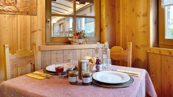 Interno di una baita in legno con un tavolo da pranzo apparecchiato per due, caratterizzato da una tovaglia a quadretti, piatti, posate e barattoli di conserve.