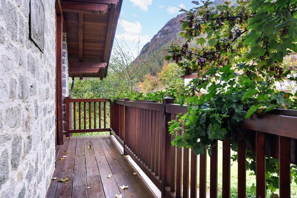 Una terraza de madera con un muro de piedra, barandilla de madera y vistas a un paisaje montañoso.