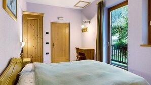 A bedroom with a bed, a desk, a chair, a window with a view of greenery, and a door.