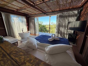 A bedroom with a large bed, a bathtub, a TV, and a balcony with a view.